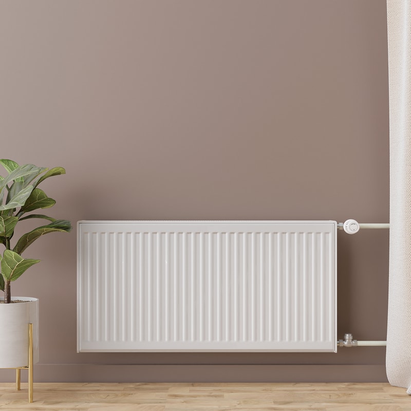 Radiateur panneau blanc sur un mur beige clair, près d'une plante en pot et d'un rideau crème