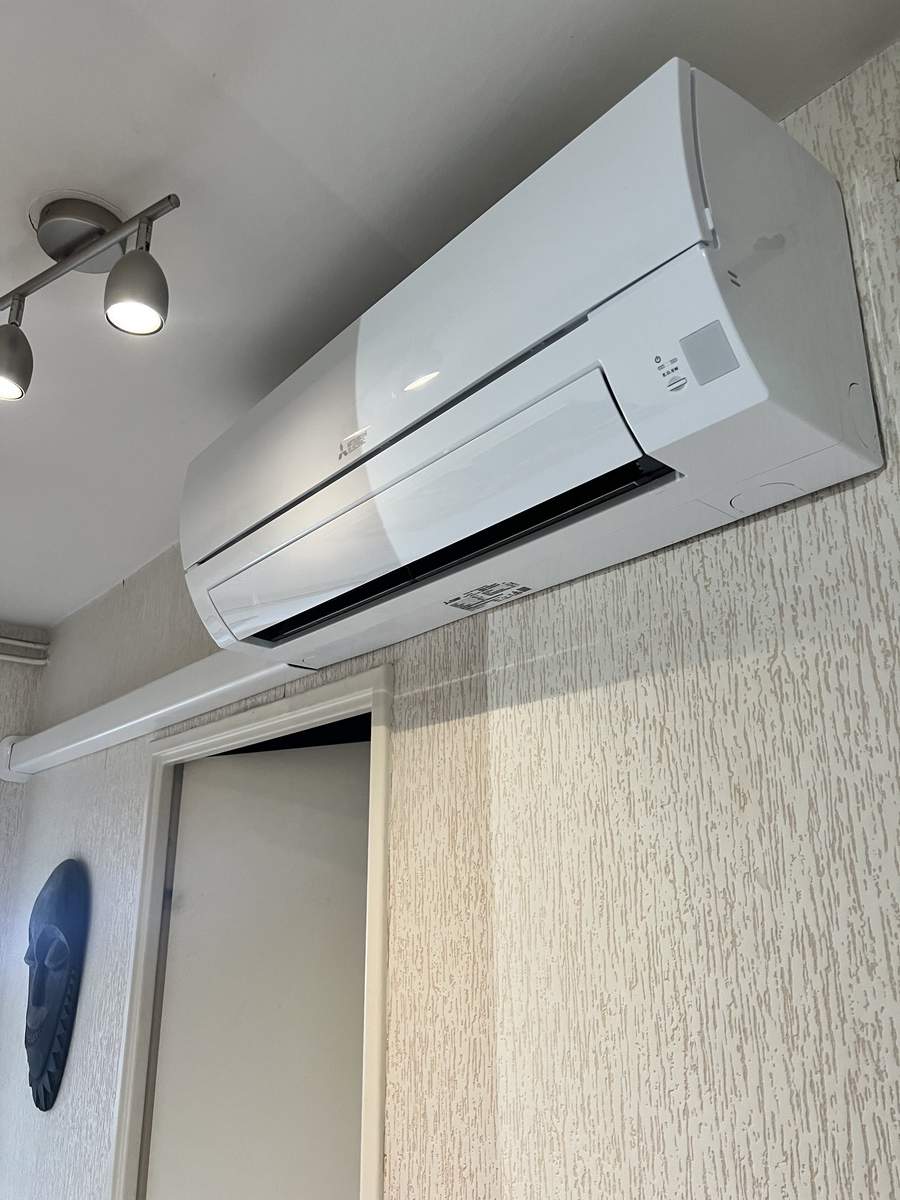 Climatisation Mitsubishi Electric : Installation Murale Climatiseur mural Mitsubishi Electric blanc installé sur un mur beige texturé au-dessus d'un encadrement de porte.