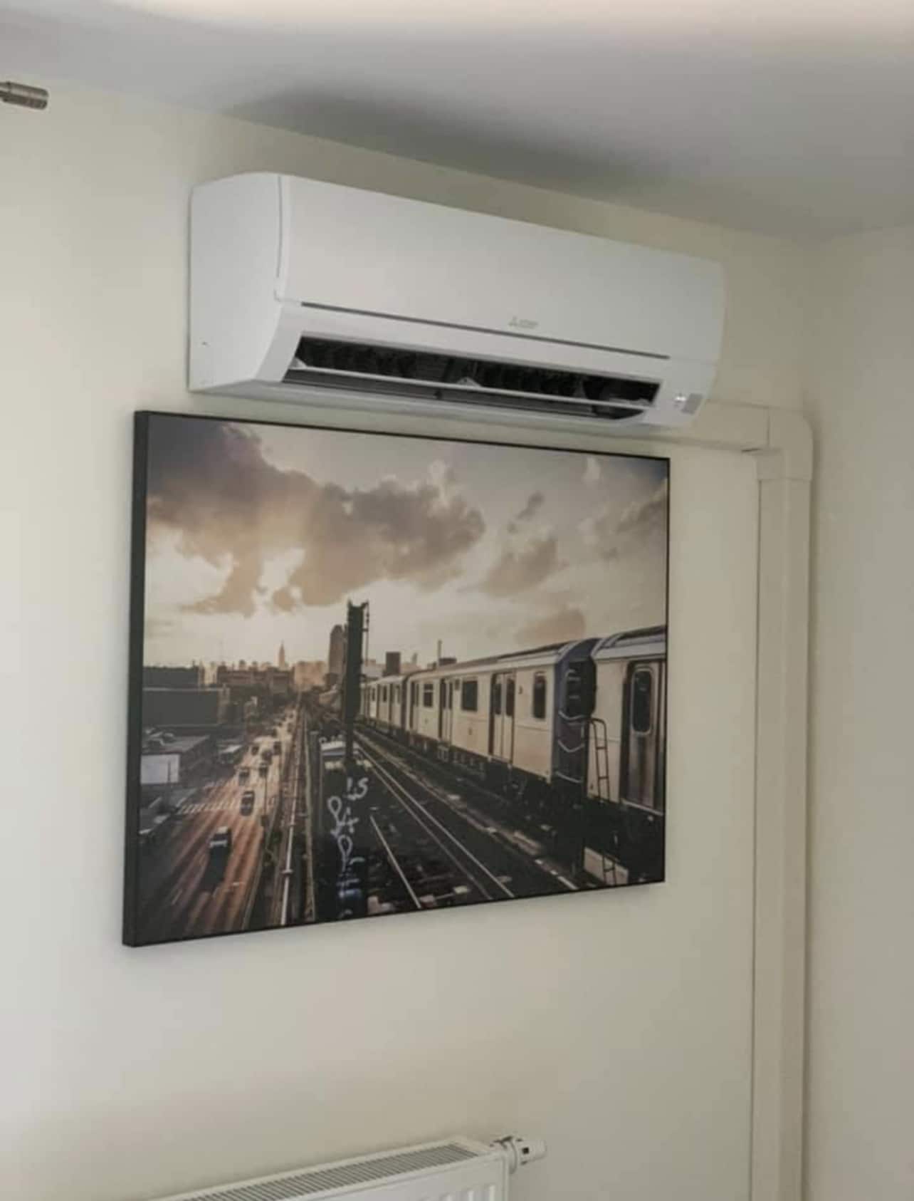 Climatisation Mitsubishi et décoration murale urbaine Climatiseur Mitsubishi blanc installé au-dessus d'un tableau de métro urbain au coucher du soleil sur un mur blanc.